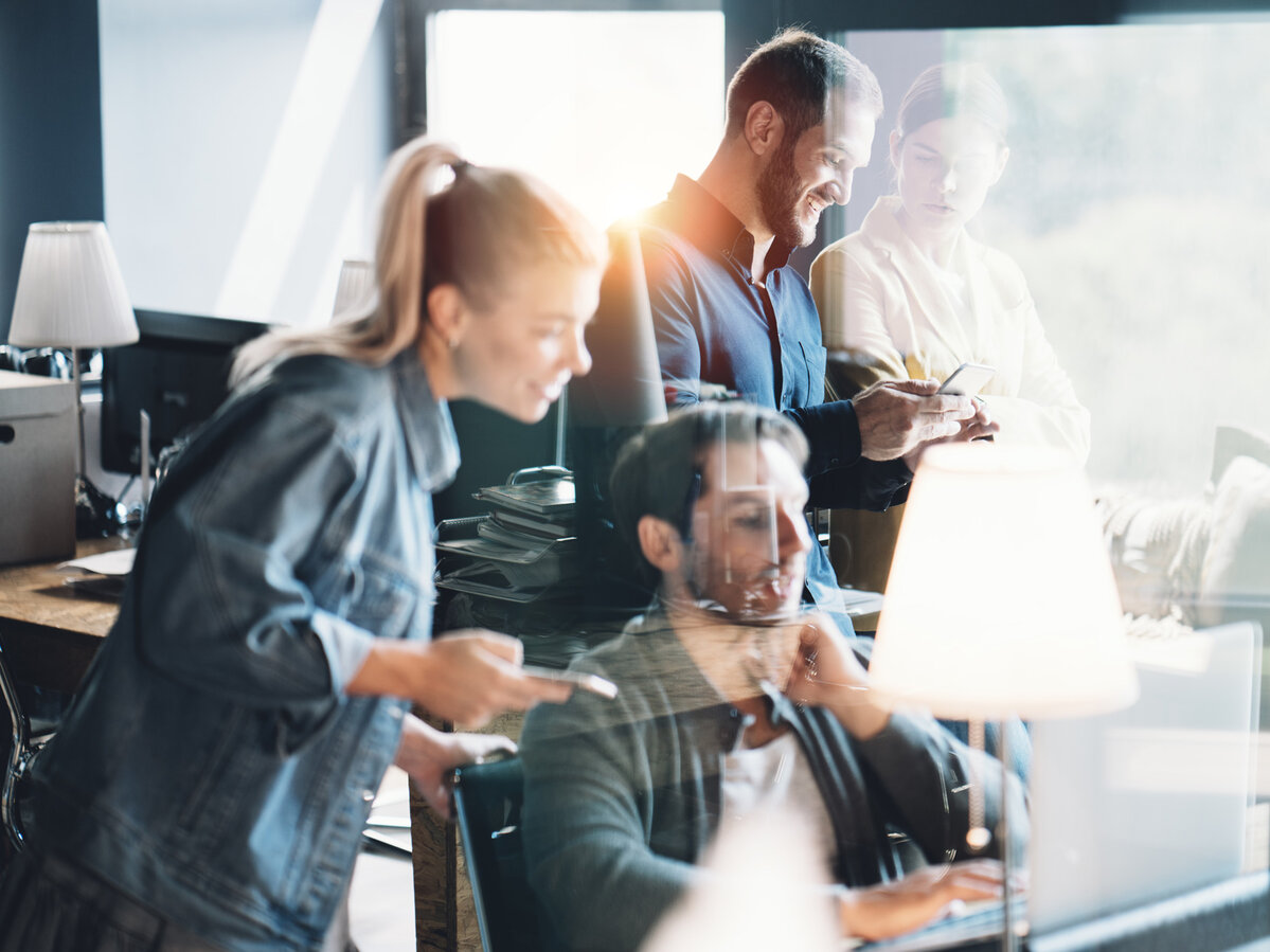 Ein Team von vier Personen arbeitet gemeinsam in einem Büro, teils mit Smartphones und Laptops.