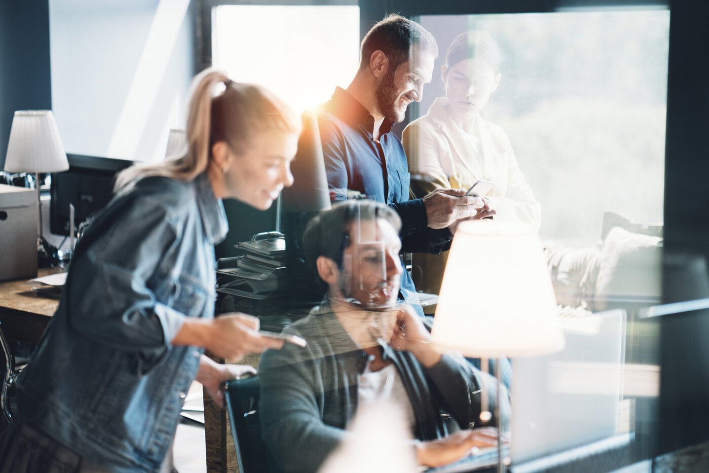 Ein Team von vier Personen arbeitet gemeinsam in einem Büro, teils mit Smartphones und Laptops.