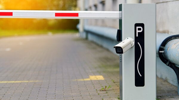 Automatische Schrankenanlage für die Parkplatzverwaltung mit Überwachungskamera. Automatisches Sicherheitstor mit gestreiftem Schrankenarm und integrierter Überwachungskamera, das den Zugang zum privaten Parkplatzbereich beschränkt