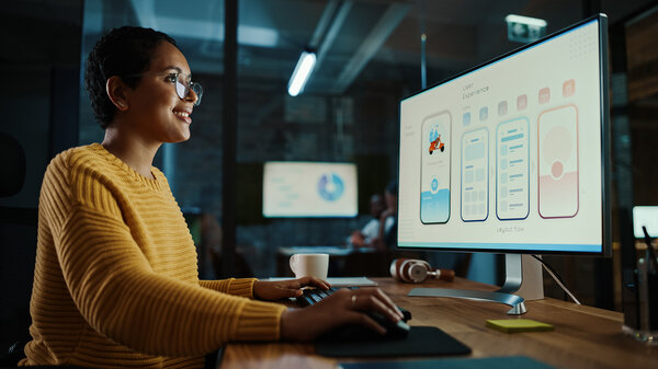 Junge Designerin arbeitet an einem Desktop-Computer in einem kreativen Büro.  Frau entwickelt ein neues App-Design und eine Benutzeroberfläche in einer Software zur Bearbeitung digitaler Grafiken.