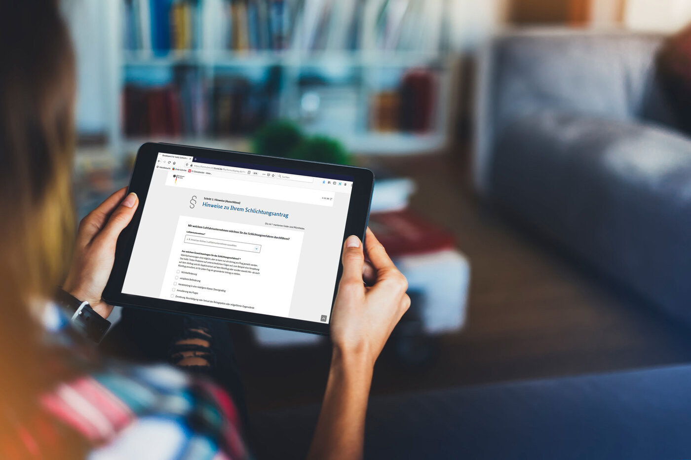 Eine Person hält ein Tablet, auf dem eine Website mit dem Titel 'Hinweise zu Ihrem Schlichtungsantrag' angezeigt wird.