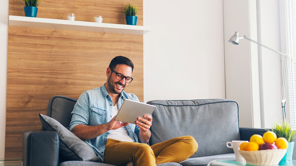Mann mit Brille auf der Couch in modernem Wohnzimmer nutzt das Tablet