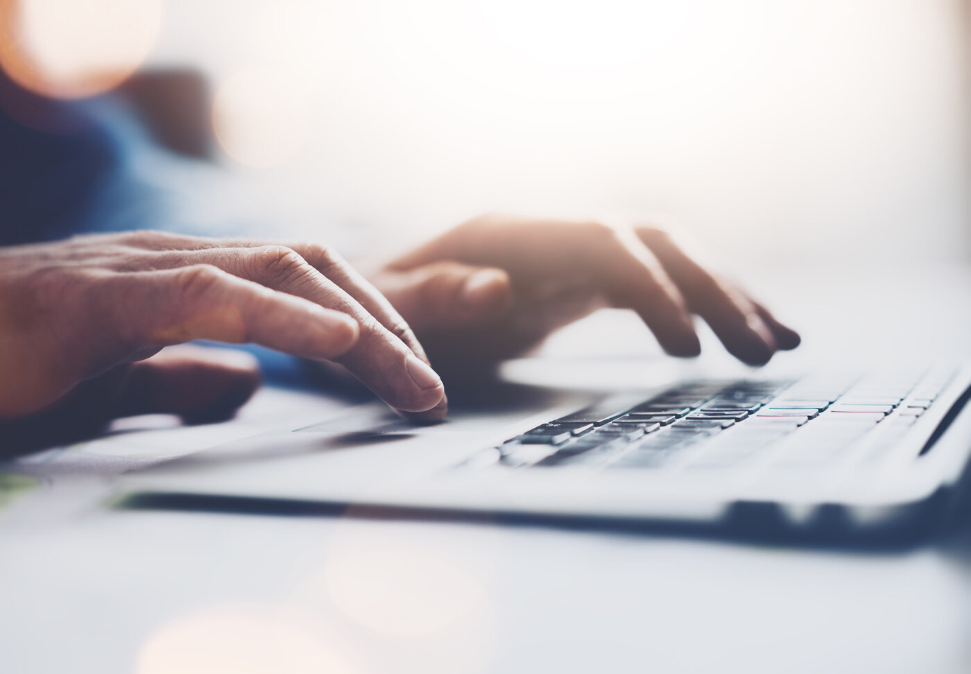 Eine Nahaufnahme von Händen, die auf einer Laptop-Tastatur tippen, symbolisiert digitale Kommunikation und moderne Arbeitsmethoden.