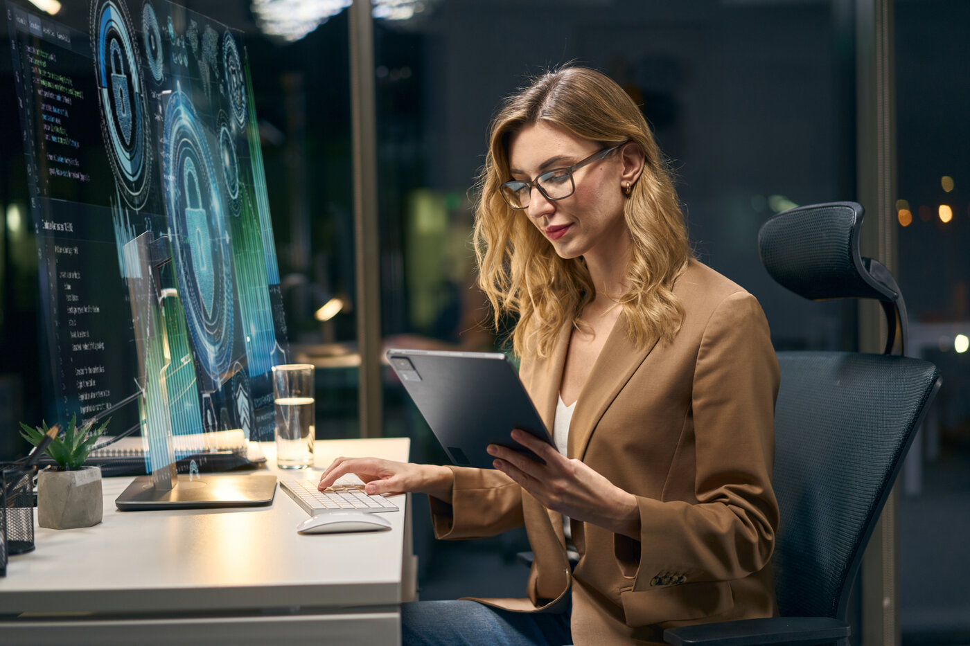 Fachfrau analysiert Daten auf einem Bildschirm und einem Tablet in einem modernen Arbeitsumfeld.
