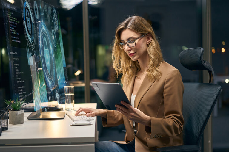 Fachfrau analysiert Daten auf einem Bildschirm und einem Tablet in einem modernen Arbeitsumfeld.