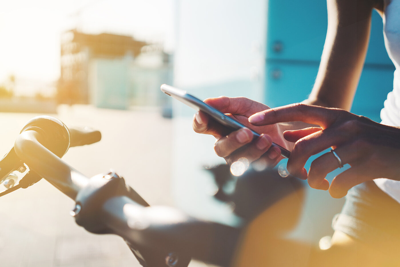 Eine Person bedient ein Smartphone, während sie an einem Fahrradlenker steht, in einer sonnigen Umgebung.