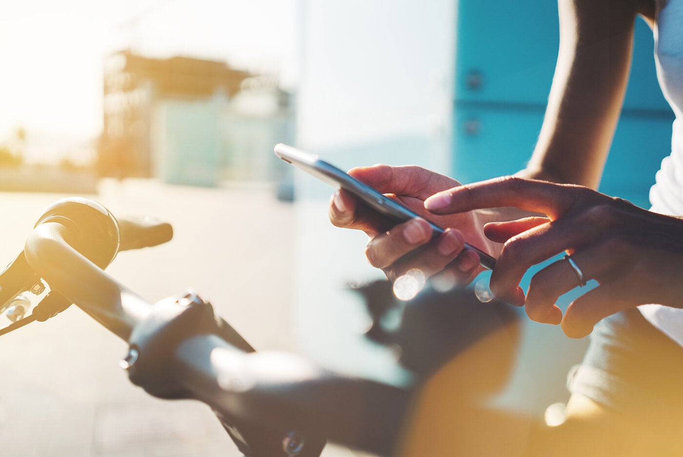 Eine Person bedient ein Smartphone, während sie an einem Fahrradlenker steht, in einer sonnigen Umgebung.