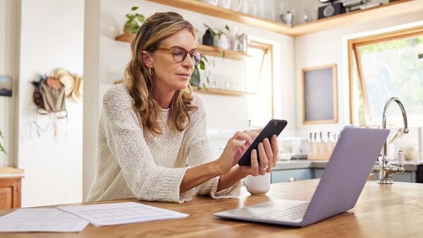 Eine Frau, die zu Hause oder in der Küche mit einem Laptop oder einer Fintech-App für die Finanzplanung, die Anlagebuchhaltung oder Versicherungssteuern arbeitet. Eine reife Person, die sich mit Technologie, Unterlagen oder Dokumenten für einen Altersvorsorgekredit auskennt