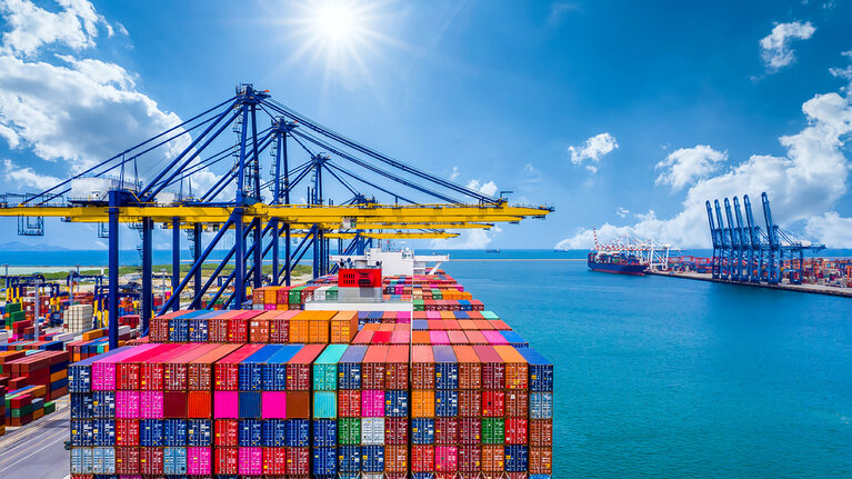 Ein Containerhafen mit farbigen Containern und Kränen unter blauem Himmel bei Sonnenschein.