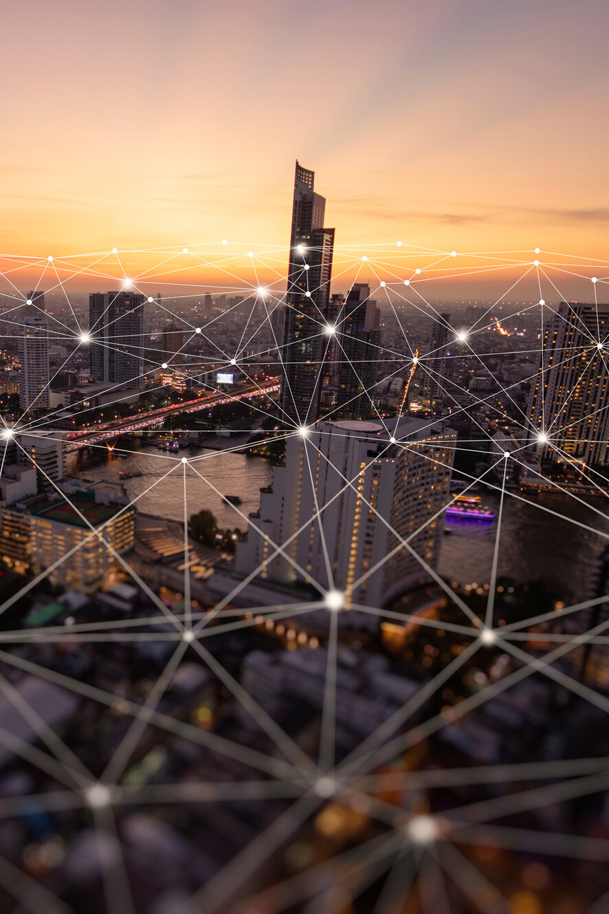Eine Stadtansicht bei Sonnenuntergang, verbunden durch ein digitales Netzwerk mit leuchtenden Knotenpunkten, das die digitale Vernetzung und Smart-City-Konzepte symbolisiert.