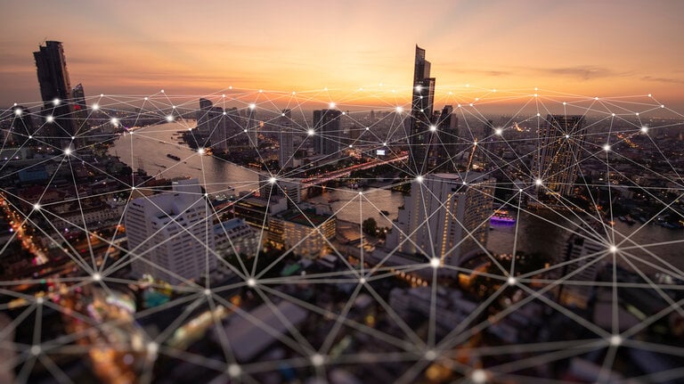Eine Stadtansicht bei Sonnenuntergang, verbunden durch ein digitales Netzwerk mit leuchtenden Knotenpunkten, das die digitale Vernetzung und Smart-City-Konzepte symbolisiert.