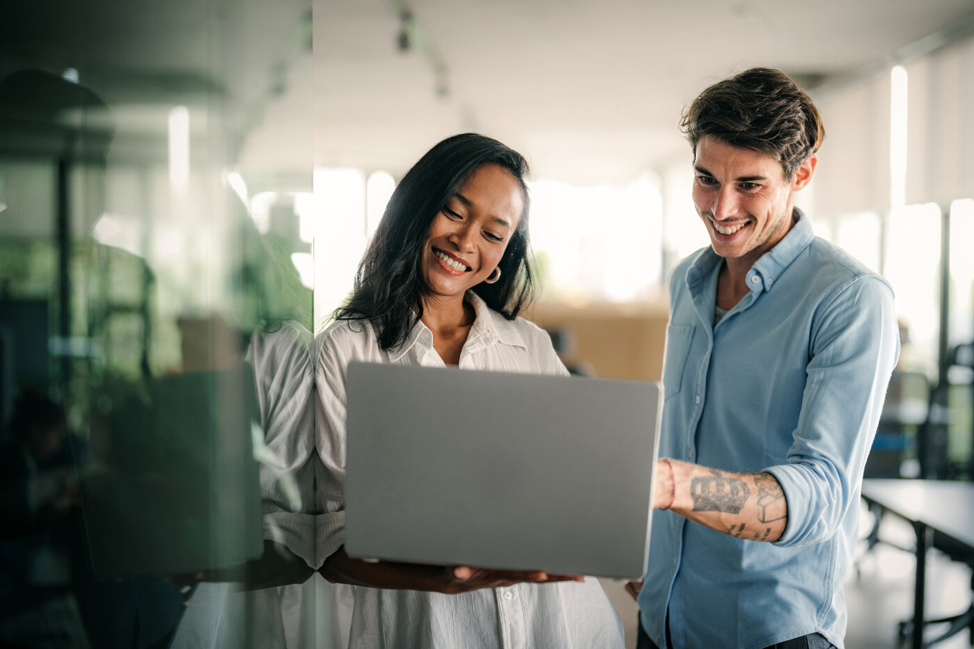 Auf dem Bild sieht man zwei Personen in einem modernen Arbeitsumfeld, wie sie an einem Laptop gemeinsam arbeiten. Eine Darstellung von Kollaboration und moderner Technologieeinsatz im Kontext generativer KI.