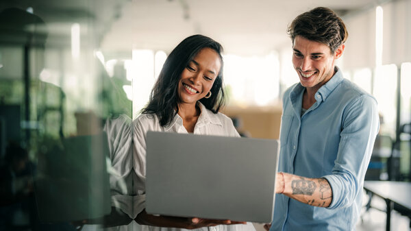 Auf dem Bild sieht man zwei Personen in einem modernen Arbeitsumfeld, wie sie an einem Laptop gemeinsam arbeiten. Eine Darstellung von Kollaboration und moderner Technologieeinsatz im Kontext generativer KI.