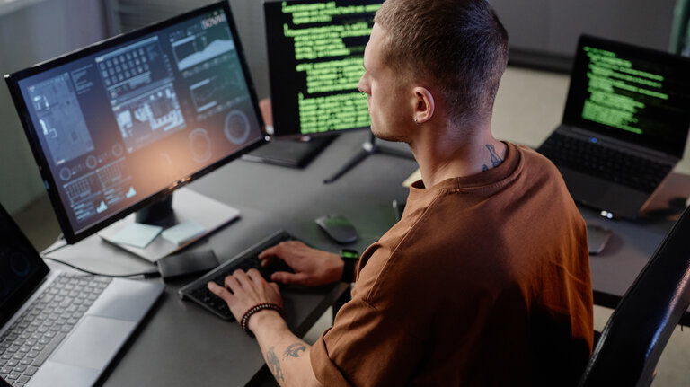Seitenansicht eines älteren IT-Entwicklers, der an seinem Schreibtisch in einem modernen Büro am Desktop-Computer arbeitet und auf der Tastatur tippt.