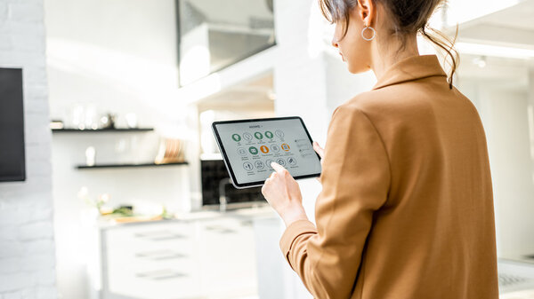Frau steuert Smart-Home-Geräte über ein digitales Tablet mit gestarteter Anwendung im weißen Wohnzimmer. Konzept für ein intelligentes Zuhause