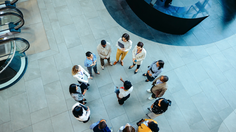 Das Team versammelt sich in einer kreisförmigen Formation in der Lobby eines modernen Bürogebäudes