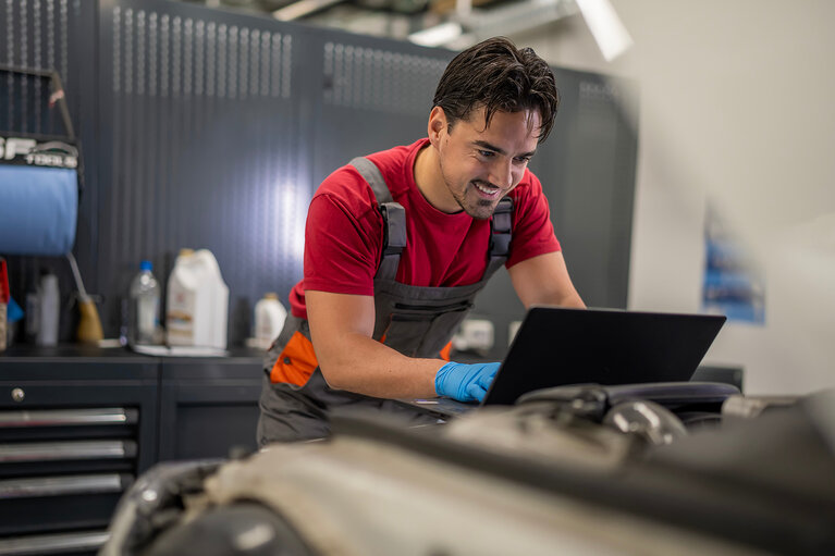 Mechaniker, der in einer Werkstatt mithilfe eines Laptops eine Diagnose am Automotor durchführt 
