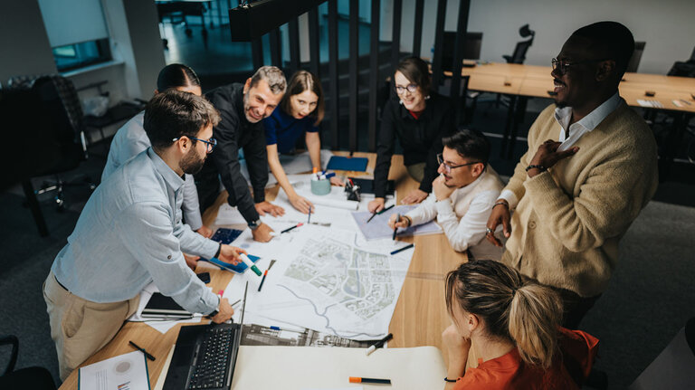 Eine vielfältige Gruppe von Geschäftsleuten versammelt sich um einen Konferenztisch und diskutiert lebhaft Ideen für ein Projekt und entwickelt neue Konzepte. Ein generationenübergreifendes Team, das sich auf Teamarbeit und Innovation in einem modernen Umfeld konzentriert.