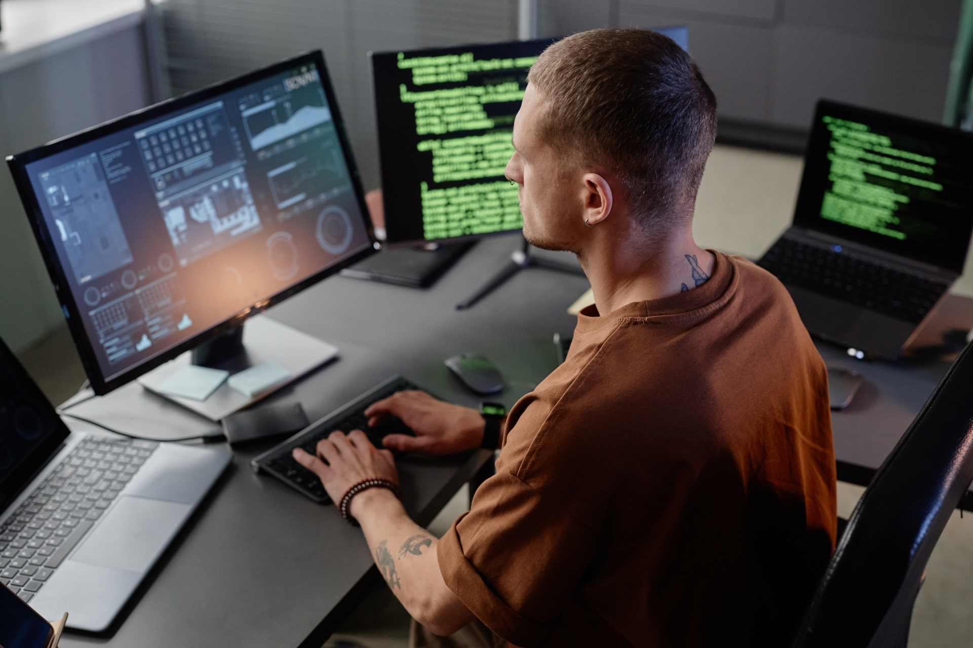 Seitenansicht eines älteren IT-Entwicklers, der an seinem Schreibtisch in einem modernen Büro am Desktop-Computer arbeitet und auf der Tastatur tippt.