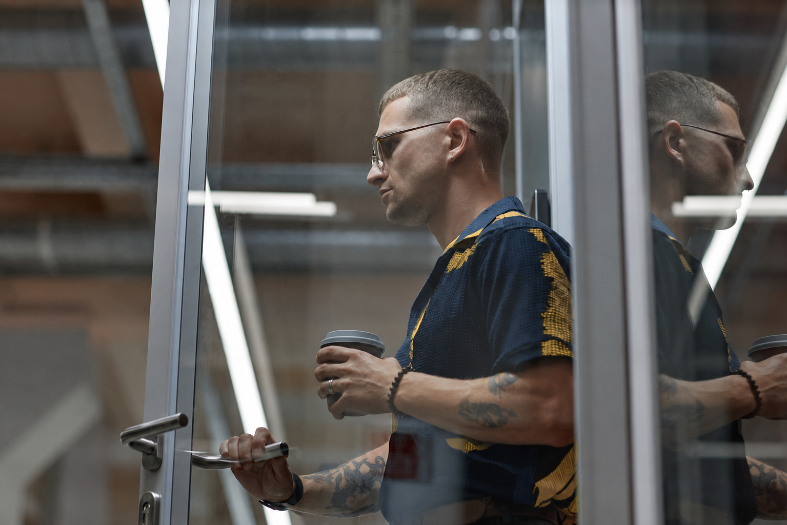Seitenansicht eines modernen Geschäftsmannes in einer Türöffnung, der mit einem wiederverwendbaren Kaffeebecher die Tür öffnet, während er das Büro in einem Coworking Space verlässt, Bildausschnitt