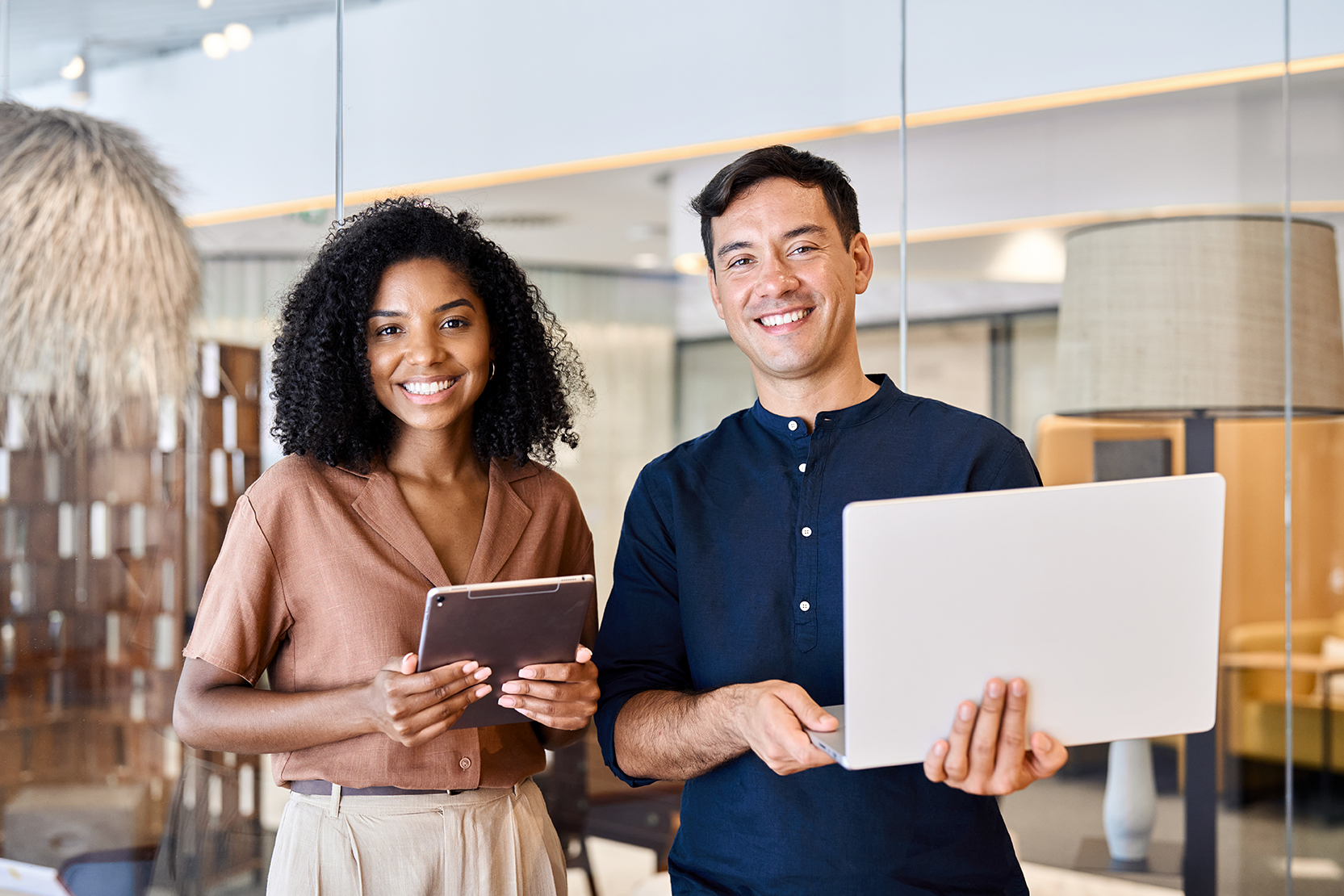 Junges, zufriedenes und professionelles Arbeitsteam – zwei selbstbewusste, vielfältige Geschäftspartner, eine Frau und ein Mann, stehen gemeinsam im Büro und blicken in die Kamera. Ein modernes, berufliches Porträt.