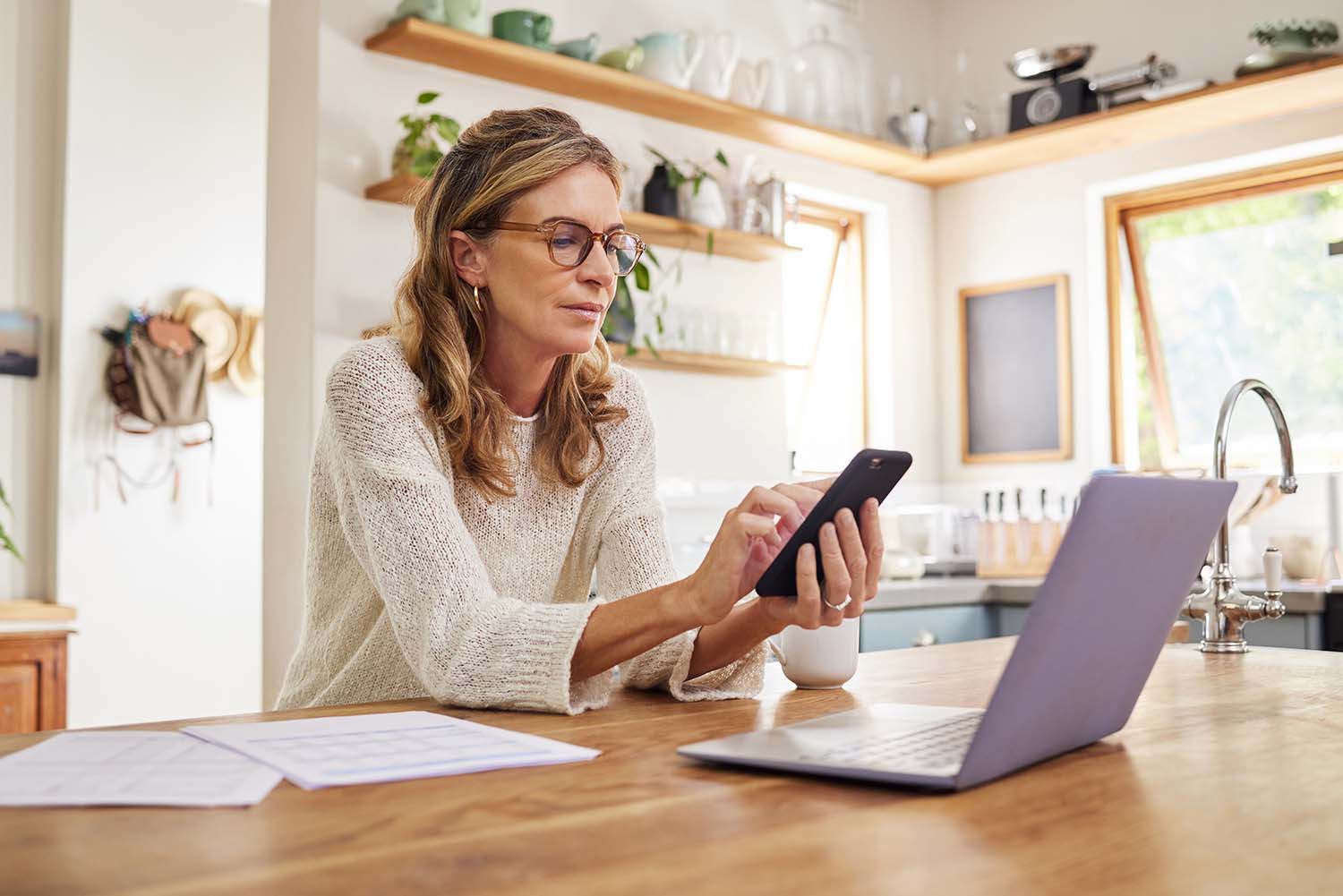 Eine Frau, die zu Hause oder in der Küche mit einem Laptop oder einer Fintech-App für die Finanzplanung, die Anlagebuchhaltung oder Versicherungssteuern arbeitet. Eine reife Person, die sich mit Technologie, Unterlagen oder Dokumenten für einen Altersvorsorgekredit auskennt